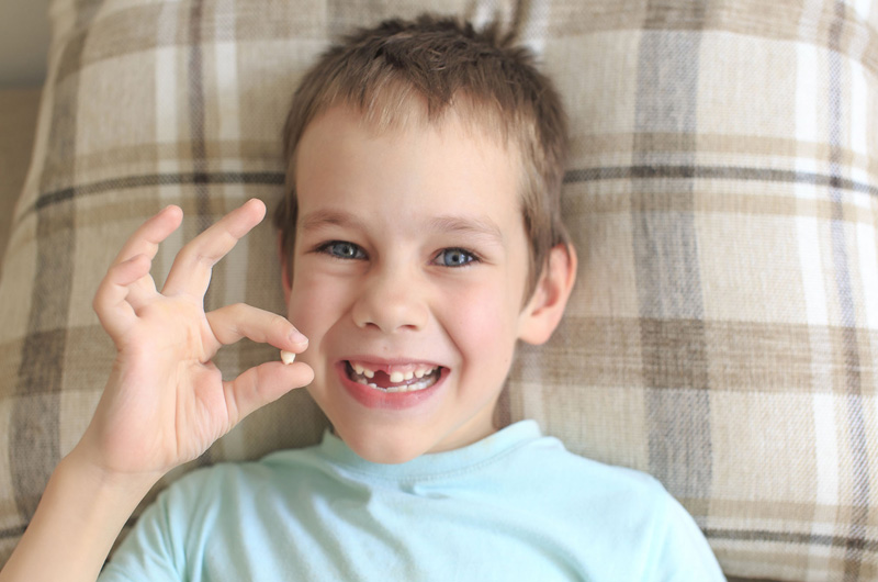 A child holding up one of his baby teeth.